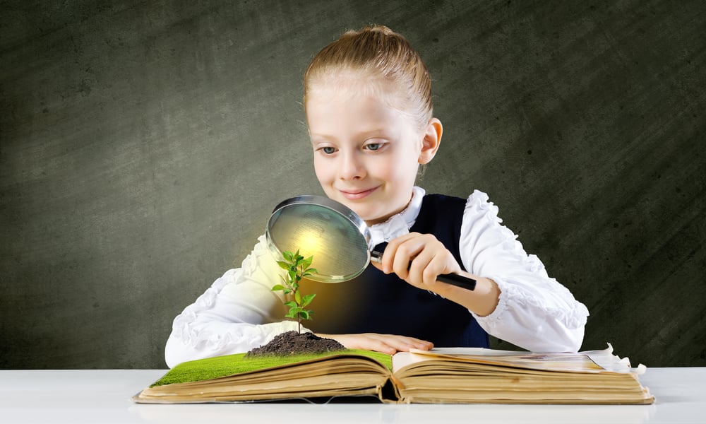 Schoolgirl examining opened book with magnifying glass